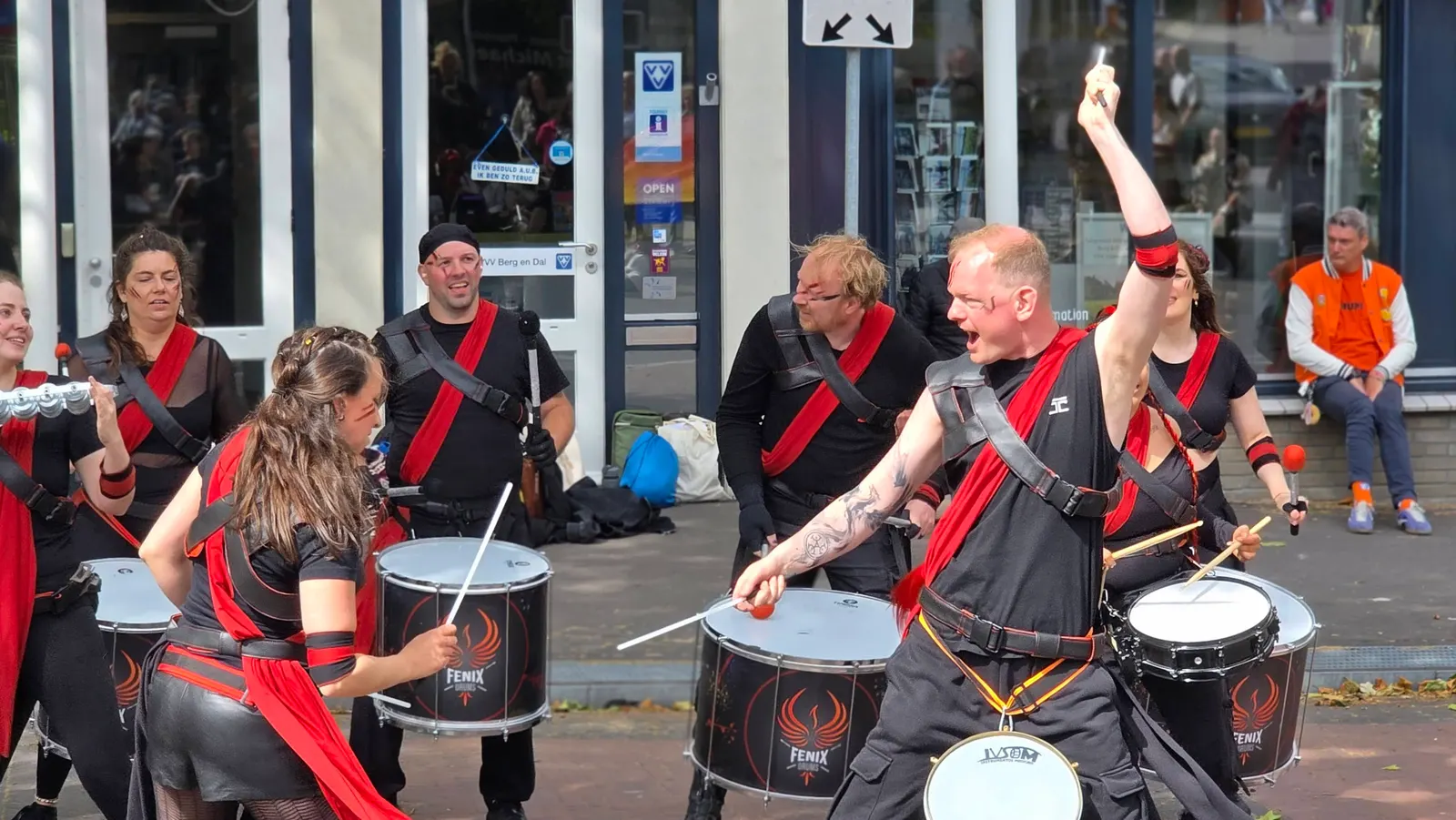 Drummer met opgeheven stok en rode banden speelt uit volle borst tijdens een optreden op straat